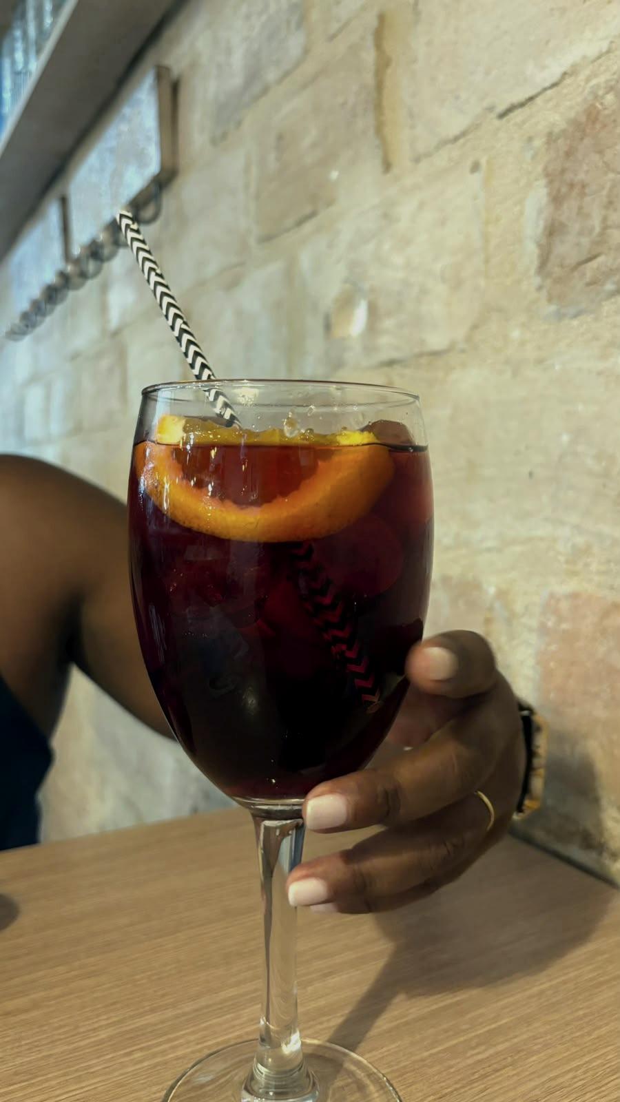 Um copo de sangria com uma fatia de laranja, na mão.